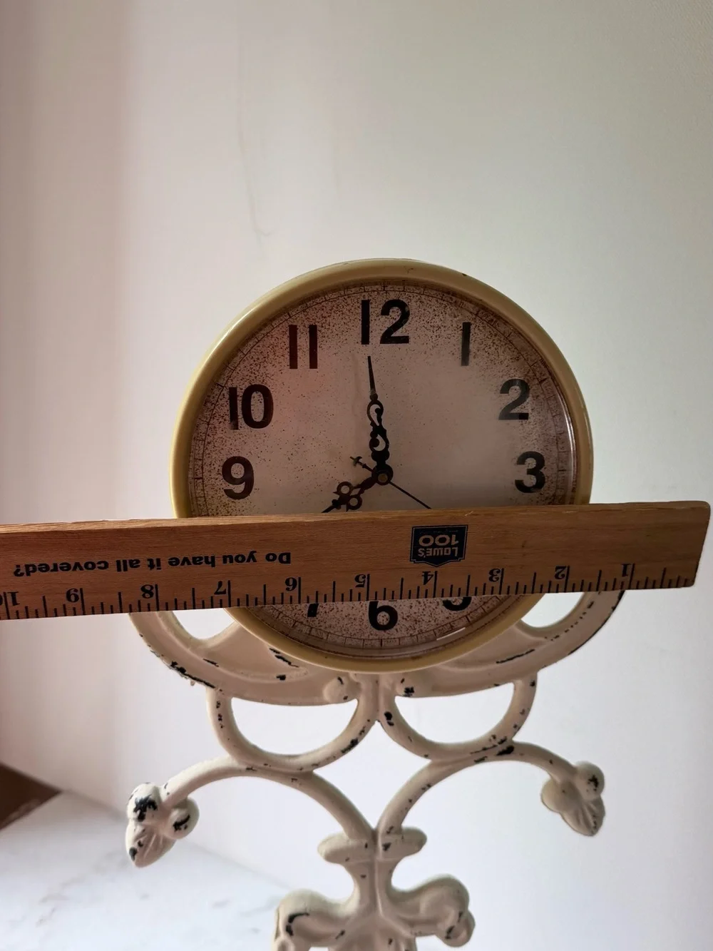 This vintage-style table clock features a distressed cream iron stand